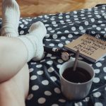 Person relaxing with tea, notebook, and polka dot bedding, creating a cozy atmosphere indoors.
